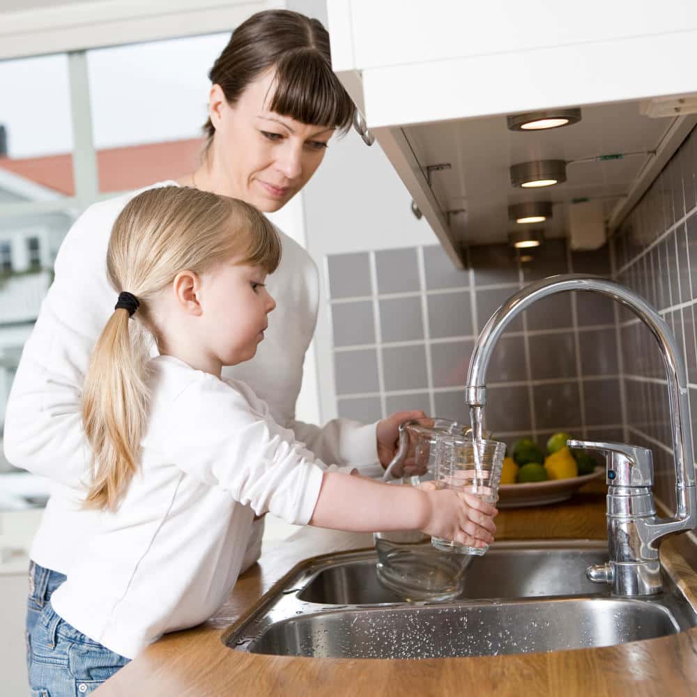 Small Girl in the kitchen with her mother drinking water