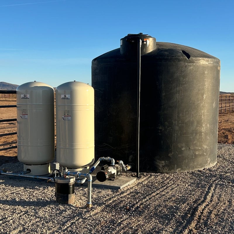 Well pump installation with water storage tank, submersible pump, and irrigation pump system